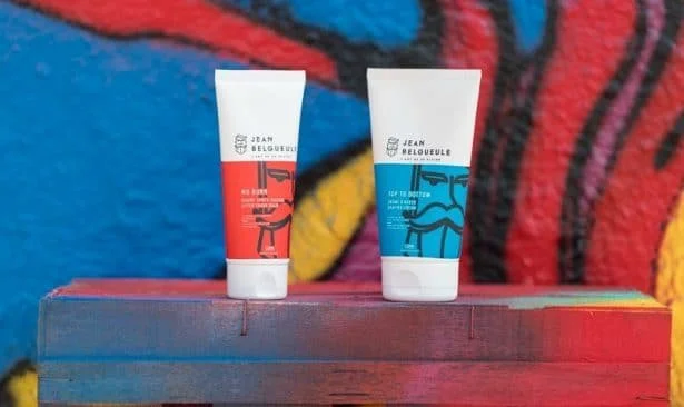 Deux tubes de crème de Jean Belgueule, l’un rouge et l’autre bleu, posés sur une surface colorée devant un fond de graffiti.