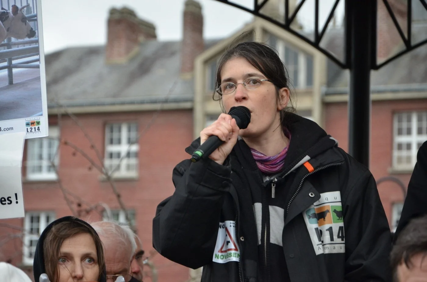 Une femme avec des lunettes tient un microphone et parle lors d’une manifestation en plein air contre la ferme des 1000 vaches.