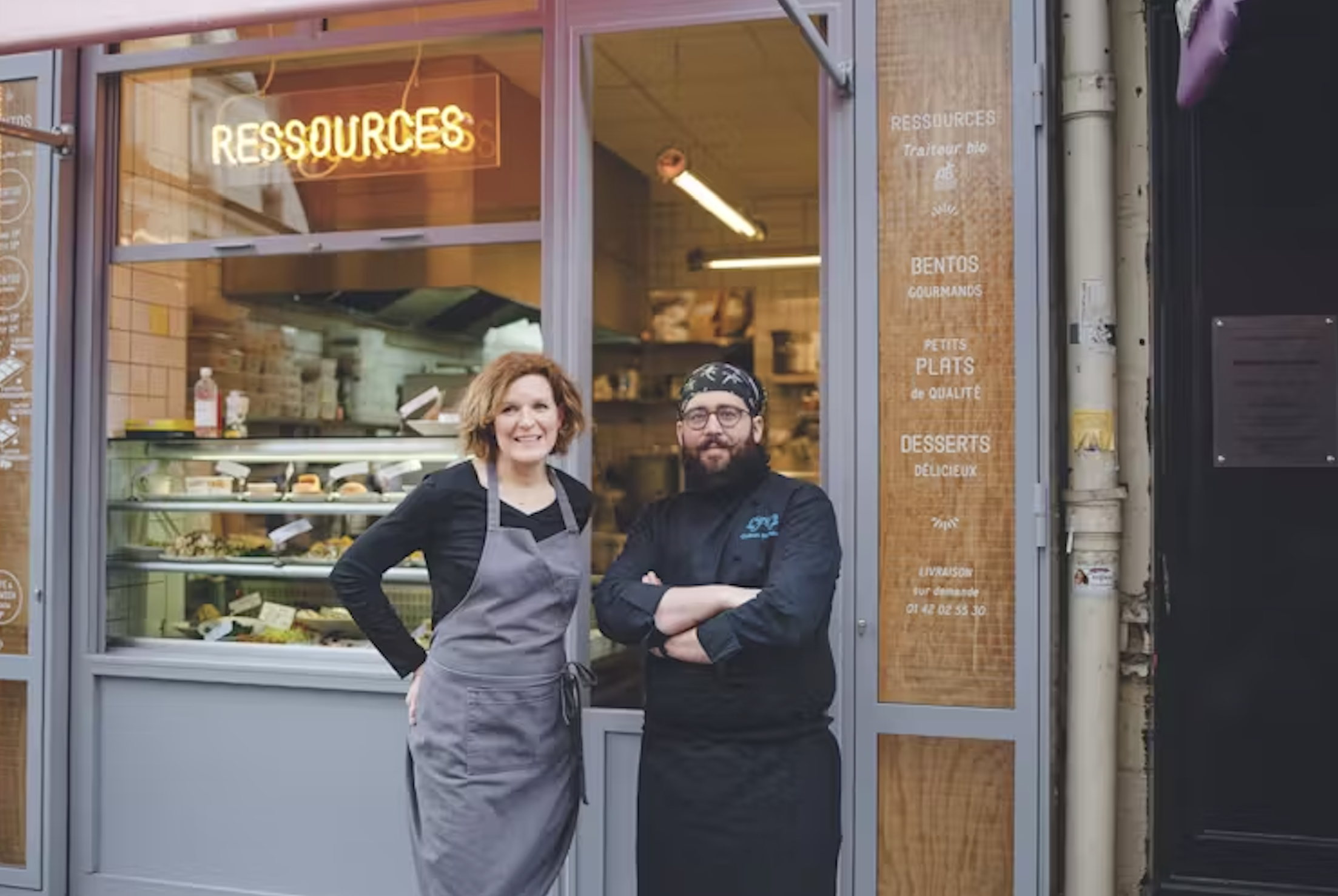 Deux chefs posent devant la vitrine d’une boutique de restauration à Paris, avec un néon 'Ressources' au-dessus d’eux.