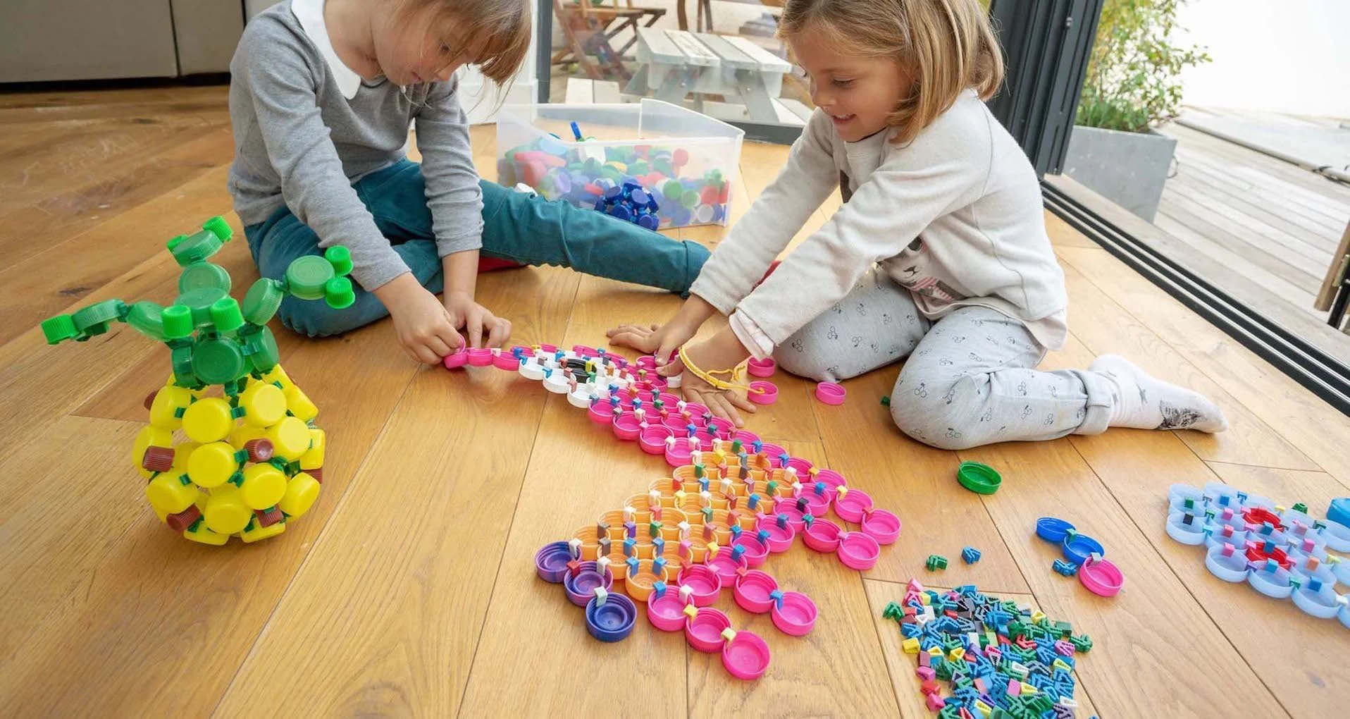 Deux enfants jouant avec des jouets de construction en plastique colorés sur un sol en bois.